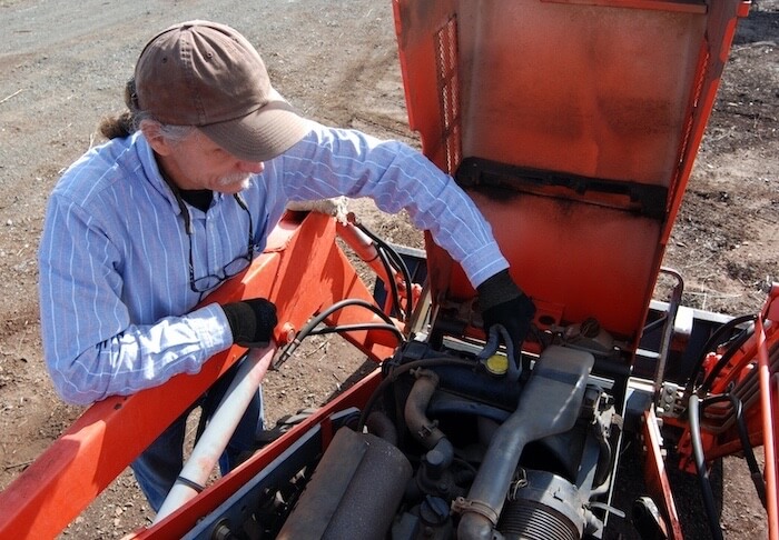 Man servicing farming equipment with tractor hydraulic fluid